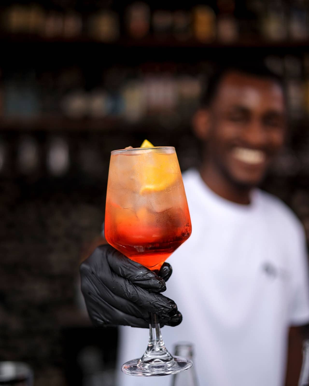 A smiling bartender holding out an Aperol spritz
