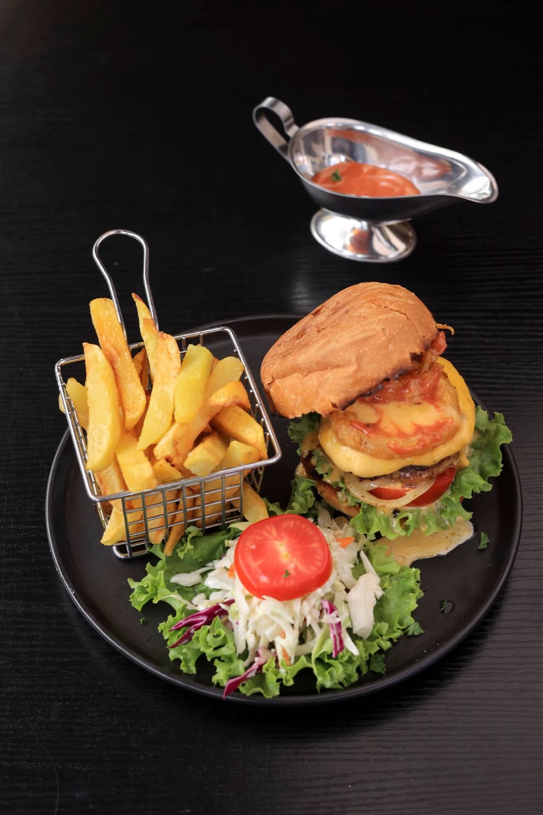 Burger, fries and salad on a black plate with sauce