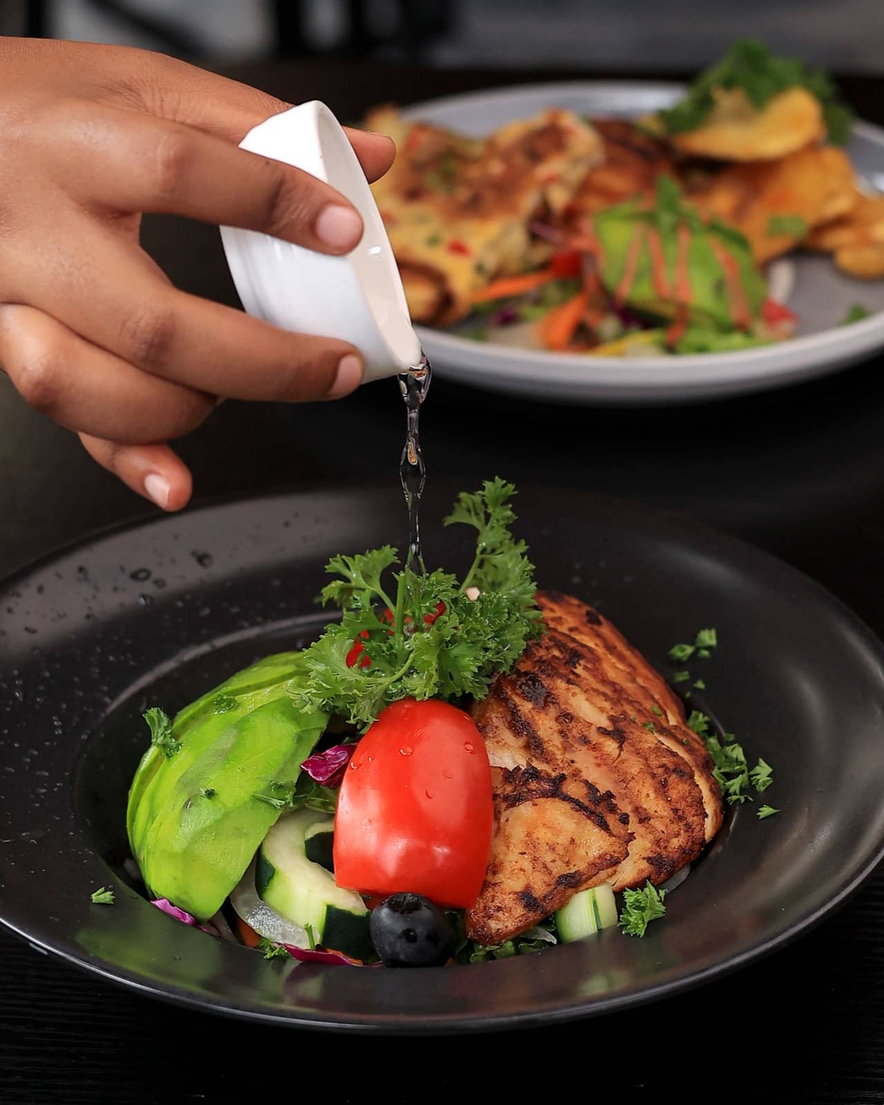 A hand pouring dressing over a grilled chicken salad
