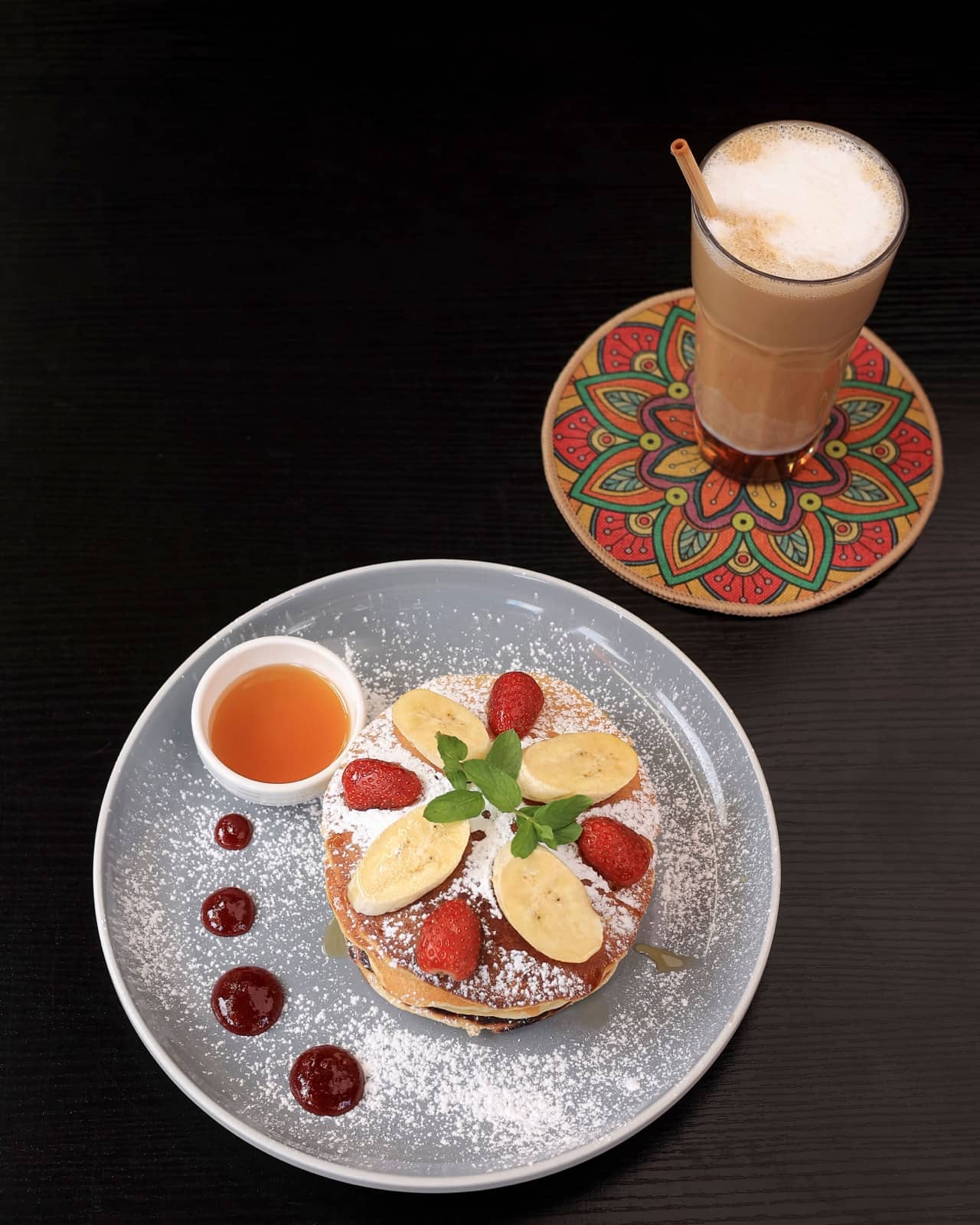 Pancakes next to an iced latte on a patterned coaster