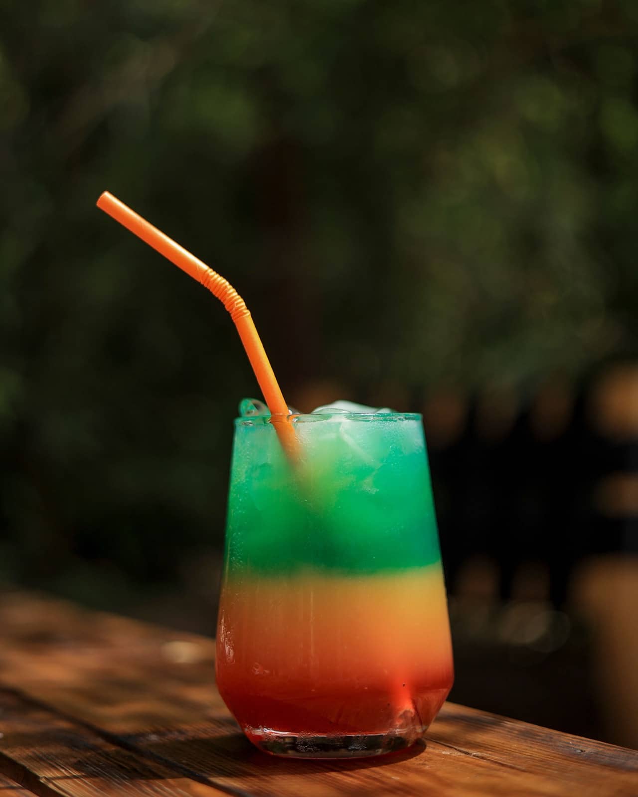Layered green, orange and red cocktail with a straw
